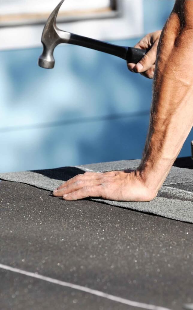 worker using hammer on shingles vertical