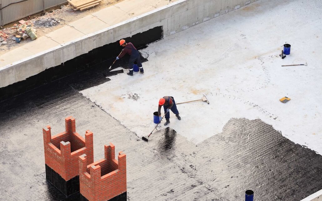 Image from above of men painting waterproofing substance onto commercial roof