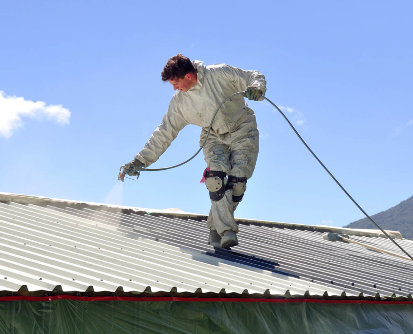 View of roofer using spray coating on metal roof